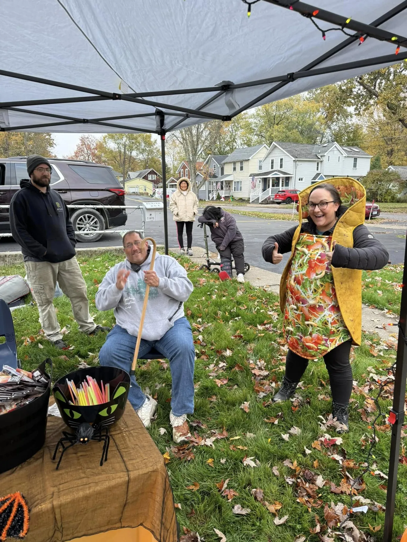 TFMC volunteers share candy at an outdoor fall neighborhood event; one volunteer wears a taco costume.