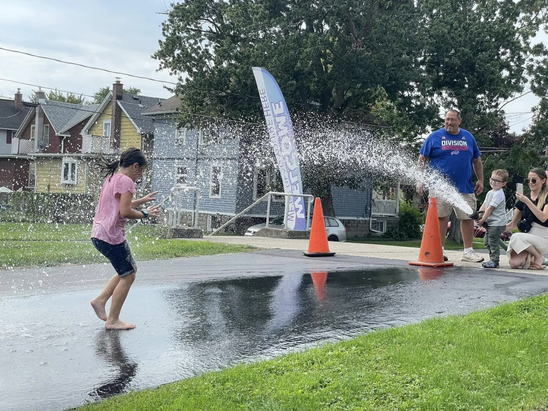 A child runs through water spray while family members smile at a TFMC neighborhood event.